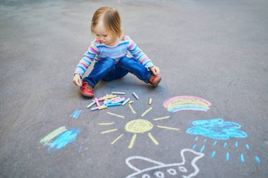 Asfalta renkli tebeşirler çizen sevimli küçük kız. Küçük çocuklar için açık hava aktiviteleri ve yaratıcı oyunlar