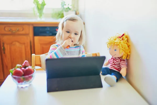愛らしい幼児の女の子は新鮮なイチゴを食べ タブレットを使用しています 子供の漫画を食べながら見ている 子供の教育におけるデジタル技術 — ストック写真