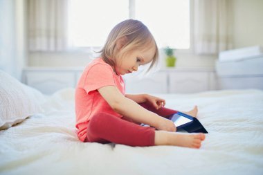 Evde dijital tableti olan küçük bir kız. Çocuk çizgi film izliyor. Çocuk arkadaşlarıyla ya da anaokulu öğrencileriyle iletişim kurmak için alet kullanıyor. Çocuklar için eğitim ve uzak mesafe eğitimi. Evde kalıp eğlenin.