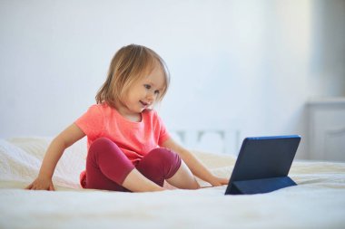 Evde dijital tableti olan küçük bir kız. Çocuk çizgi film izliyor. Çocuk arkadaşlarıyla ya da anaokulu öğrencileriyle iletişim kurmak için alet kullanıyor. Çocuklar için eğitim ve uzak mesafe eğitimi. Evde kalıp eğlenin.