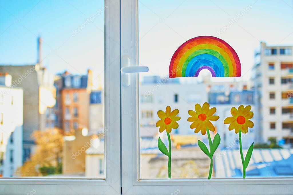Colorful rainbow and yellow flowers painted on window glass in Parisian apartment, view to residential buildings with Eiffel tower in the background. Self isolation, social distancing and quarantine in Paris, France