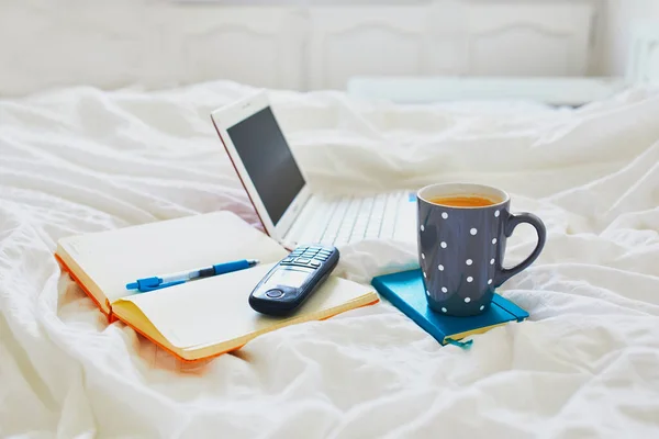 ノートパソコン コーヒーカップ ノートブック 携帯電話のベッドの上できれいな白いリネン 家の概念からのフリーランス 距離学習や仕事 — ストック写真