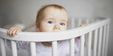 Ebeveyn yatağına bağlı, birlikte uyuyan sevimli bir kız bebek. Küçük çocuk karyolada oturuyor.