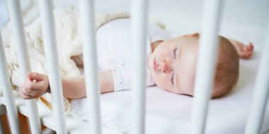 Sevimli bir kız bebek, anne babasının yatağına bağlı olarak birlikte yattığı karyolada uyuyor. Küçük çocuk karyolada kestiriyor. Güneşli kreşte küçük bir çocuk.