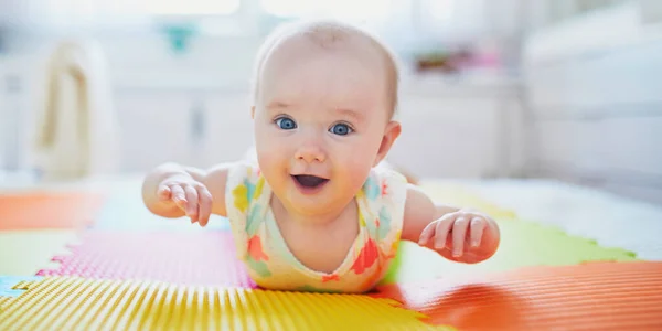 幸せな笑顔赤ちゃん女の子横たわっカラフルな遊びマット上の床にとクロールしようと — ストック写真