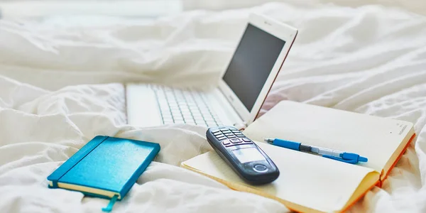 ノートパソコン ノートブック 携帯電話のベッドの上できれいな白いリネン 家の概念からのフリーランス 距離学習や仕事 — ストック写真