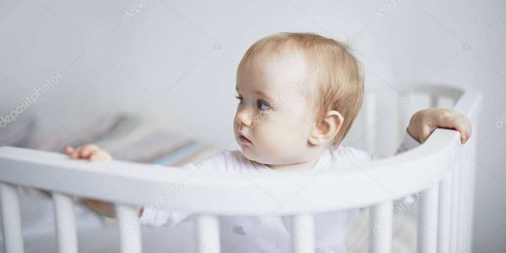 Adorable baby girl in co-sleeper crib attached to parents bed. Little kid sitting in cot