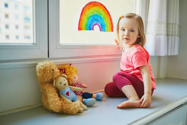 Förtjusande Liten Flicka Fästa Regnbåge Ritning Till Fönsterglas Som Tecken — Stockfoto