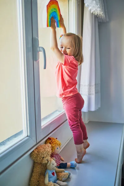 Förtjusande Liten Flicka Fästa Regnbåge Ritning Till Fönsterglas Som Tecken — Stockfoto
