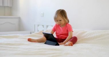 Evde dijital tableti olan küçük bir kız. Çocuk çizgi film izliyor. Çocuk arkadaşlarıyla ya da anaokulu öğrencileriyle iletişim kurmak için alet kullanıyor. Çocuklar için eğitim ve uzak mesafe eğitimi. Evde kalıp eğlenin.