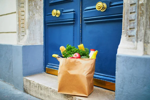 Food delivery during coronavirus outbreak. Paper bag with grocery order in front of the door in Paris, France during Covid-19 epidemic. Safe online shopping, food donation or takeout meal concept