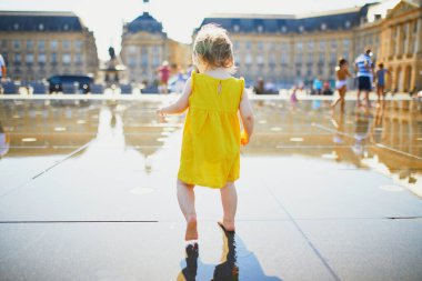 Sıcak bir yaz gününde Bordeaux, Fransa 'da ünlü açık havuzda (Miroir d' eau) eğlenen sarı elbiseli sevimli kız çocuğu. Çocuklar için yaz etkinlikleri