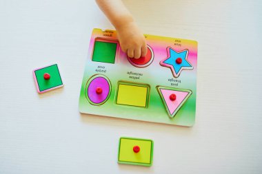 Küçük kız ya da oğlan tahta yapboz yapıyor. Çocuk geometrik şekiller öğreniyor. Çocuk sorunları çözmeyi ve bilişsel beceriler geliştirmeyi öğreniyor