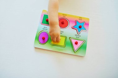 Küçük kız ya da oğlan tahta yapboz yapıyor. Çocuk geometrik şekiller öğreniyor. Çocuk sorunları çözmeyi ve bilişsel beceriler geliştirmeyi öğreniyor