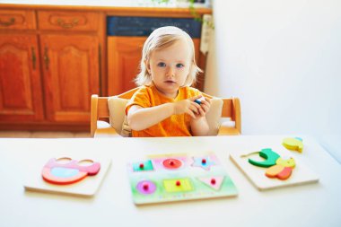 Ahşap yapboz yapan sevimli küçük kız. Çocuk geometrik şekiller öğreniyor. Çocuk sorunları çözmeyi ve bilişsel beceriler geliştirmeyi öğreniyor