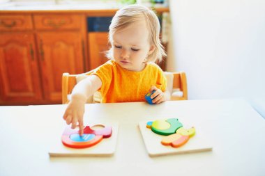 Ahşap yapboz yapan sevimli bir kız, kafası karışmış görünüyor, sonra ne yapacağından emin değil. Çocuk sorunları çözmeyi ve bilişsel beceriler geliştirmeyi öğreniyor