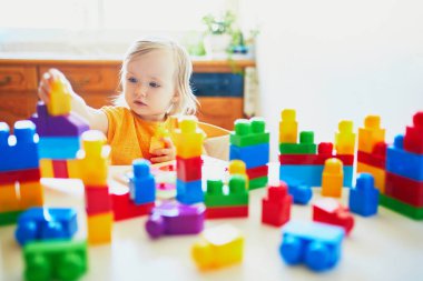 Anaokulunda ya da anaokulunda renkli plastik bloklarla oynayan sevimli küçük bir kız. Yaratıcı oyunlar ve çocuklar için ev eğlencesi