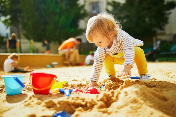 Adorable little girl on playground in sandpit. Toddler playing with sand molds and making mudpies. Outdoor creative activities for kids