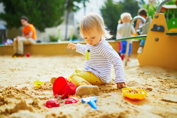 Oyun parkındaki sevimli küçük kız. Bebek kum kalıplarıyla oynuyor ve çamur yapıyor. Çocuklar için açık hava yaratıcı aktiviteler