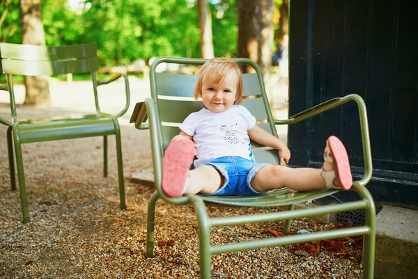Paris, Fransa 'nın Lüksemburg bahçesinde yeşil metal sandalyede oturan mutlu küçük kız.