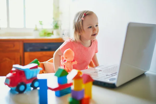 Happy toddler girl with laptop and toys. Kid using computer to communicate with friends, elderly relatives or kindergartners. Education or online communication for kids. Stay at home entertainment