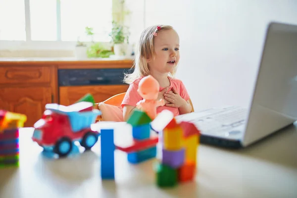 Happy toddler girl with laptop and toys. Kid using computer to communicate with friends, elderly relatives or kindergartners. Education or online communication for kids. Stay at home entertainment