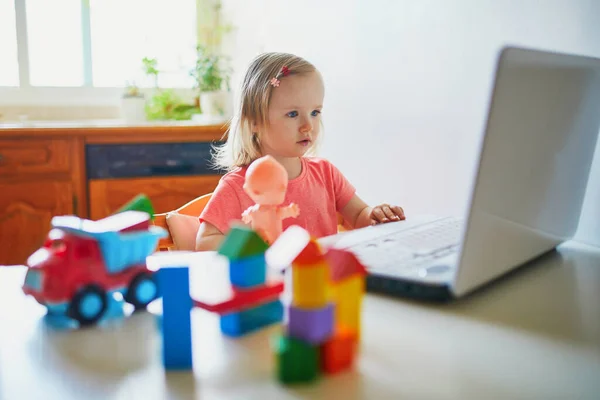 Happy toddler girl with laptop and toys. Kid using computer to communicate with friends, elderly relatives or kindergartners. Education or online communication for kids. Stay at home entertainment