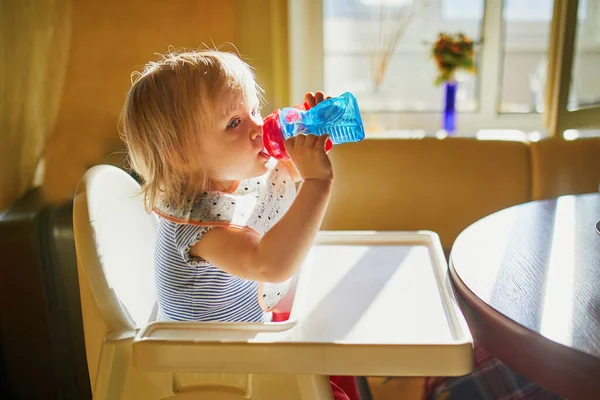 お気に入りの幼児の女の子座っている高い椅子に自宅やレストランや飲み水からシッピーカップ — ストック写真