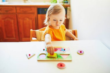 Ahşap yapboz yapan sevimli küçük kız. Çocuk geometrik şekiller öğreniyor. Çocuk sorunları çözmeyi ve bilişsel beceriler geliştirmeyi öğreniyor
