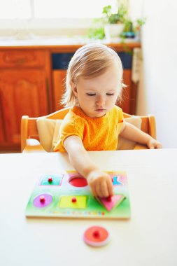Ahşap yapboz yapan sevimli küçük kız. Çocuk geometrik şekiller öğreniyor. Çocuk sorunları çözmeyi ve bilişsel beceriler geliştirmeyi öğreniyor