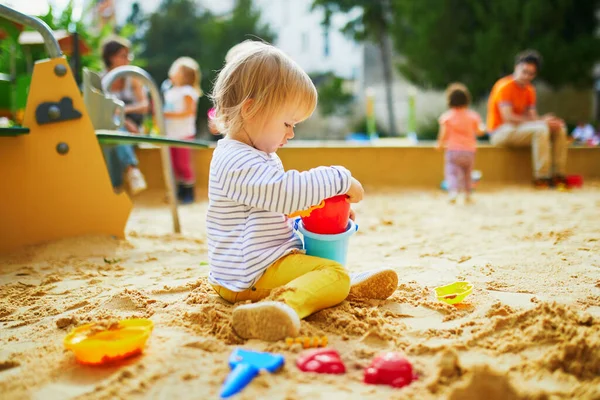 Adorable little girl on playground in sandpit. Toddler playing with sand molds and making mudpies. Outdoor creative activities for kids