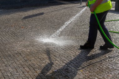 İşçi dışarıda kaldırımı sprey sıkılmış suyla yıkıyor..