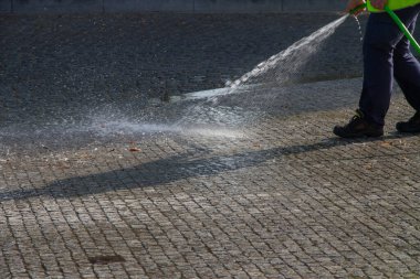 İşçi dışarıda kaldırımı sprey sıkılmış suyla yıkıyor..
