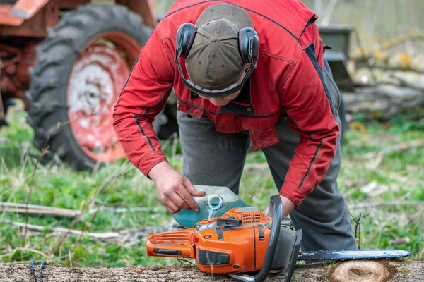 Man works by chainsaw in forest.