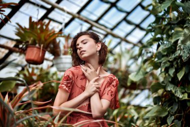 Botanik bahçesindeki güzel model kız. Makyajlı ve kırmızı elbiseli moda tarzı.