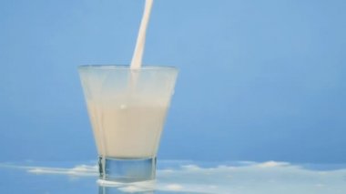 Yavaş hareket yakın çekim süt soğuk içecek içecek stüdyoda cam mavi arka plan içine döküm