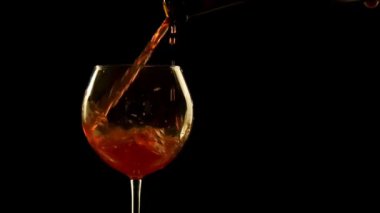 Bu video, siyah bir arka plan ile bir cam içine kırmızı şarap dökün bir özensiz ve dağınık hale anonim bir el gösterir.