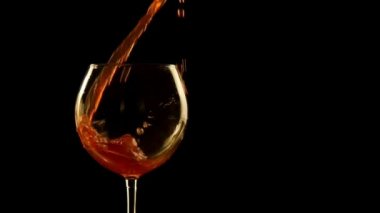 Bu video, siyah bir arka plan ile bir cam içine kırmızı şarap dökün bir özensiz ve dağınık hale anonim bir el gösterir.
