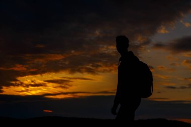Sırt çantalı yürüyüşçülerin siluetleri dağın tepesinden gün batımının tadını çıkarıyor