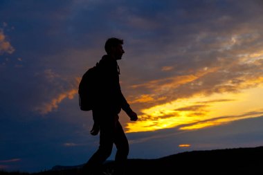 Sırt çantalı yürüyüşçülerin siluetleri dağın tepesinden gün batımının tadını çıkarıyor