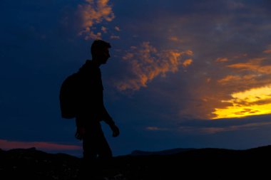Sırt çantalı yürüyüşçülerin siluetleri dağın tepesinden gün batımının tadını çıkarıyor
