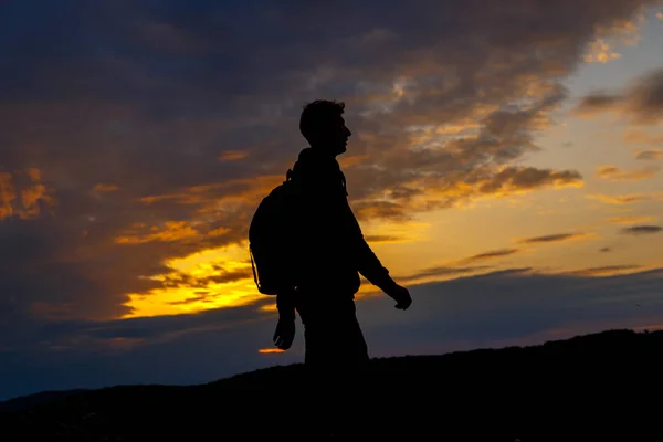 Sırt çantalı yürüyüşçülerin siluetleri dağın tepesinden gün batımının tadını çıkarıyor — Stok fotoğraf