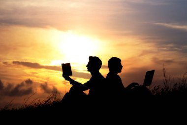 Dizüstü bilgisayarı olan bir adamın silueti ve günbatımı veya gündoğumu arka planı üzerine bir kitap.