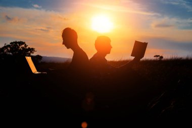 Dizüstü bilgisayarı olan bir adamın silueti ve günbatımı veya gündoğumu arka planı üzerine bir kitap.