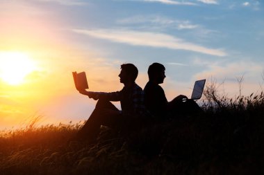 Dizüstü bilgisayarı olan bir adamın silueti ve günbatımı veya gündoğumu arka planı üzerine bir kitap.