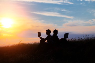 Dizüstü bilgisayarı olan bir adamın silueti ve günbatımı veya gündoğumu arka planı üzerine bir kitap.