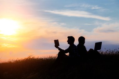 Dizüstü bilgisayarı olan bir adamın silueti ve günbatımı veya gündoğumu arka planı üzerine bir kitap.