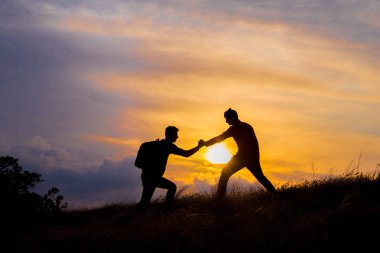 Yürüyüş yapan çift, dağlarda, gün batımında birbirlerine güven duymalarına yardımcı olur. Dağcılık takımının tepesinde birbirine yardım eden iki kişilik bir takım çalışması. Güzel bir gün batımı manzarası..