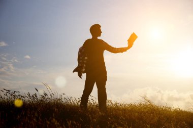 Parkta gün batımına karşı kitap okuyan bir adam. Gün batımında kitap okuyan bir adamın silueti. Sıcak ton ve yumuşak odak