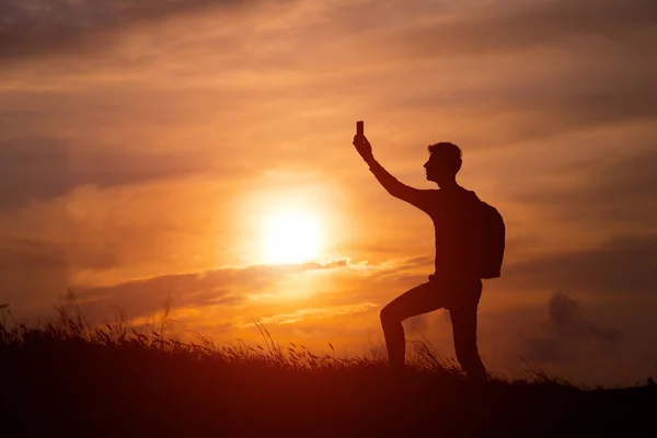 Silhouette de hombre turístico extendido de la mano en la cima de una montaña disfrutando de la puesta de sol. — Foto de Stock